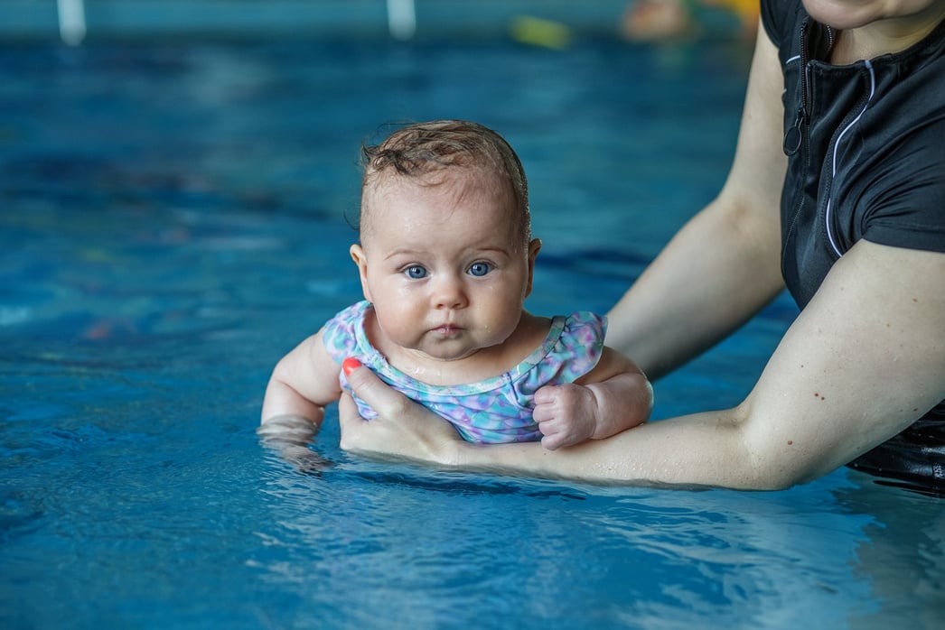 Mom supports baby with hands in swimming pool, teaches to sw